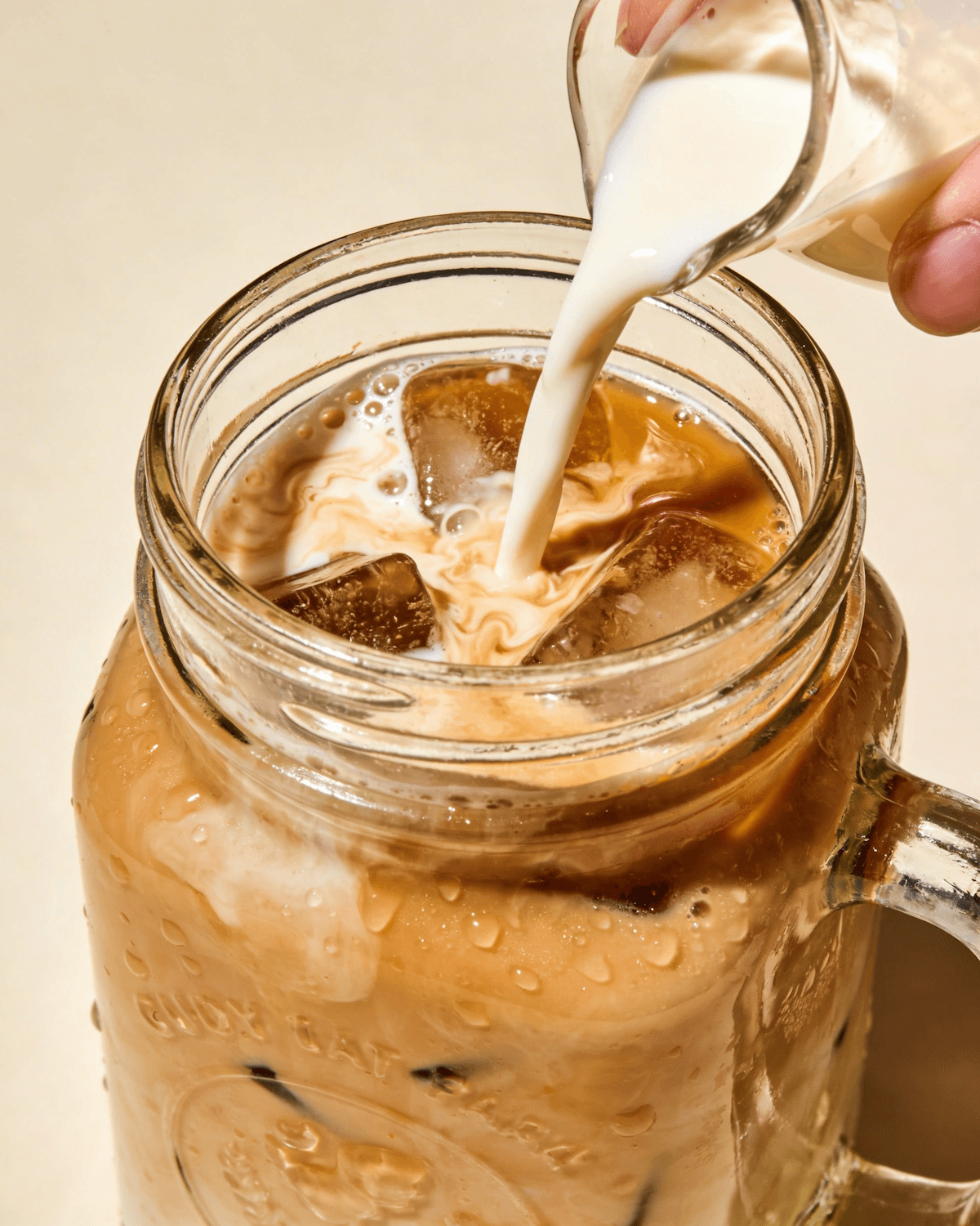 Milk being poured into a glass of iced coffee
